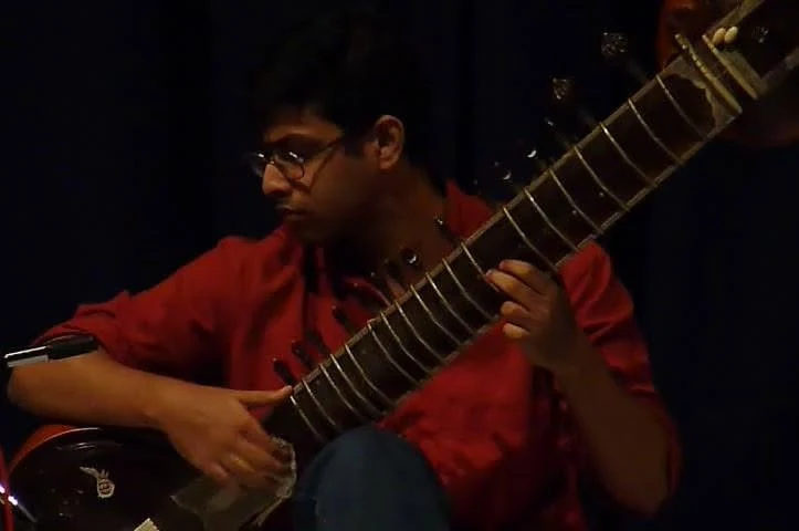 Saugata Chatterjee performing sitar in low light, in profile